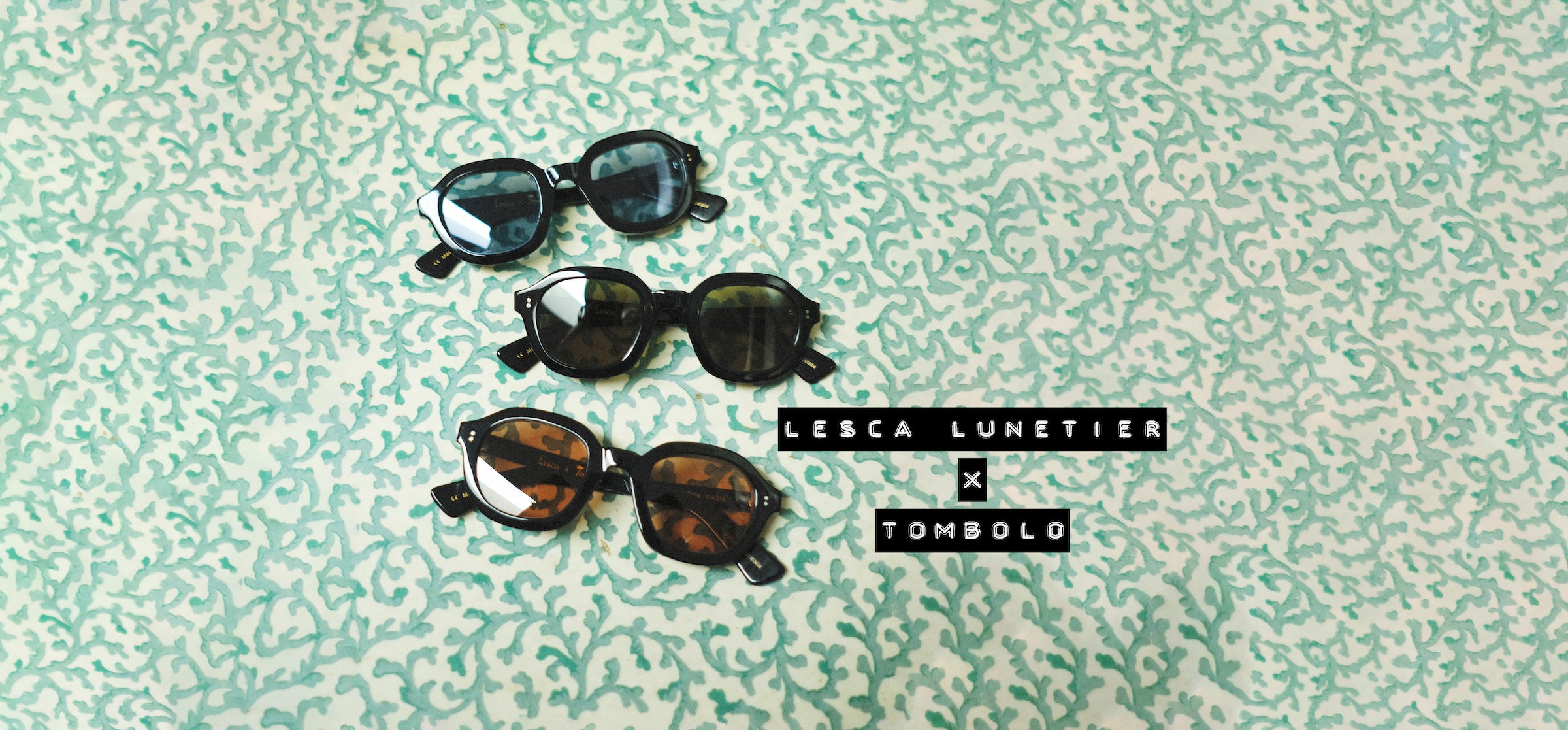 Three sunglasses with blue, green and red lenses sitting on a green coral textured background with the text 'Lesca Lunetier x Tombolo'