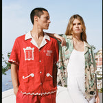 Man wearing red Le Sirenuse matching linen set while woman rests on his shoulder in the unbuttoned Liguori shirt