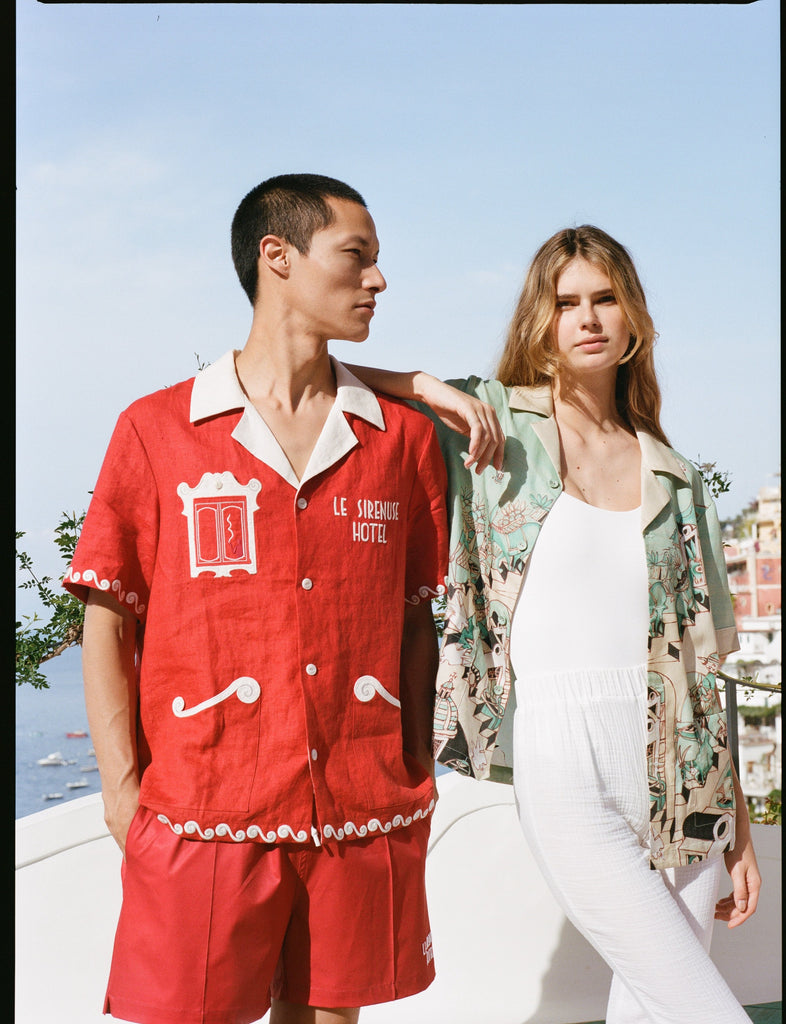Man wearing red Le Sirenuse matching linen set while woman rests on his shoulder in the unbuttoned Liguori shirt