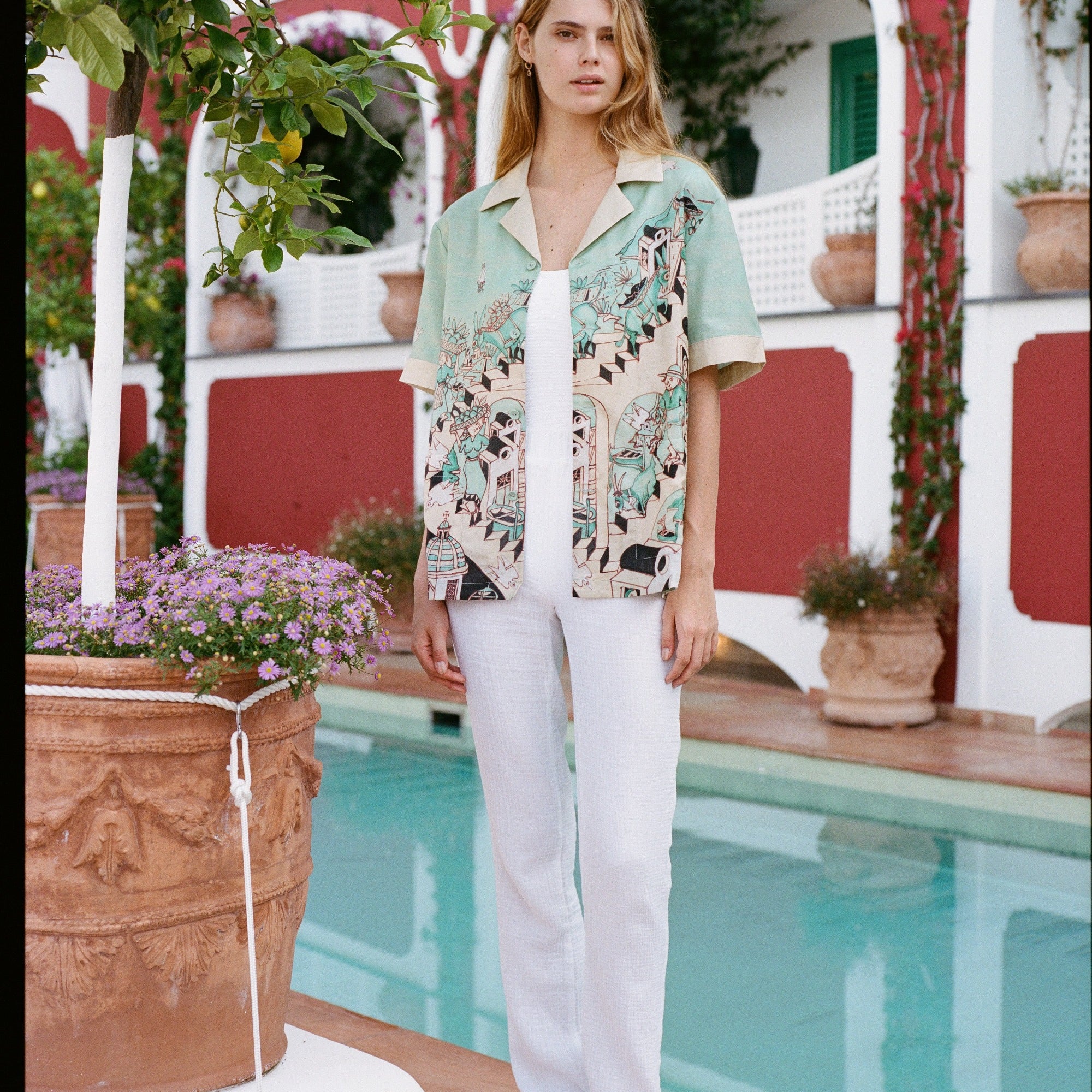 Girl wearing Liguori shirt and white pants standing in front of the pool at the Hotel Le Sirenuse