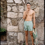 Male model wearing swim trunks and sandals smoking a cigarette