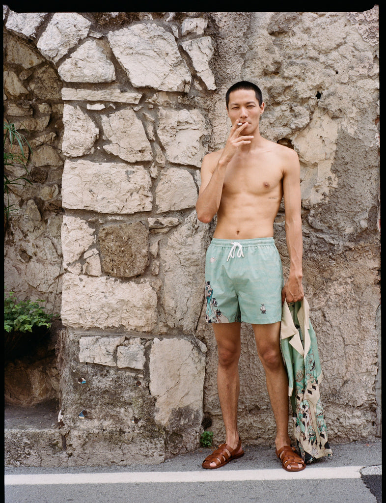 Man wearing matching shorts, holding shirt in one hand while smoking with the other