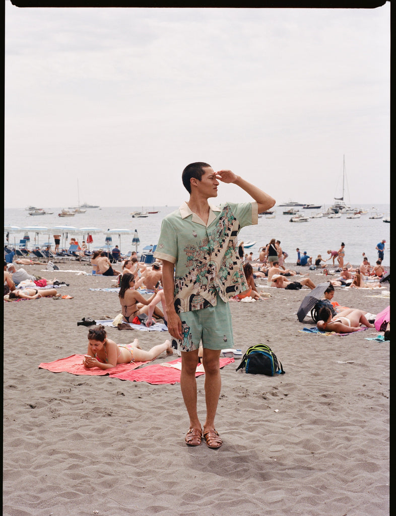Male model wearing full set on a crowded beach looking right with his hand shielding the sun from his eyes