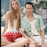 man and woman staring at the camera on a boat with the positano landscape in the background