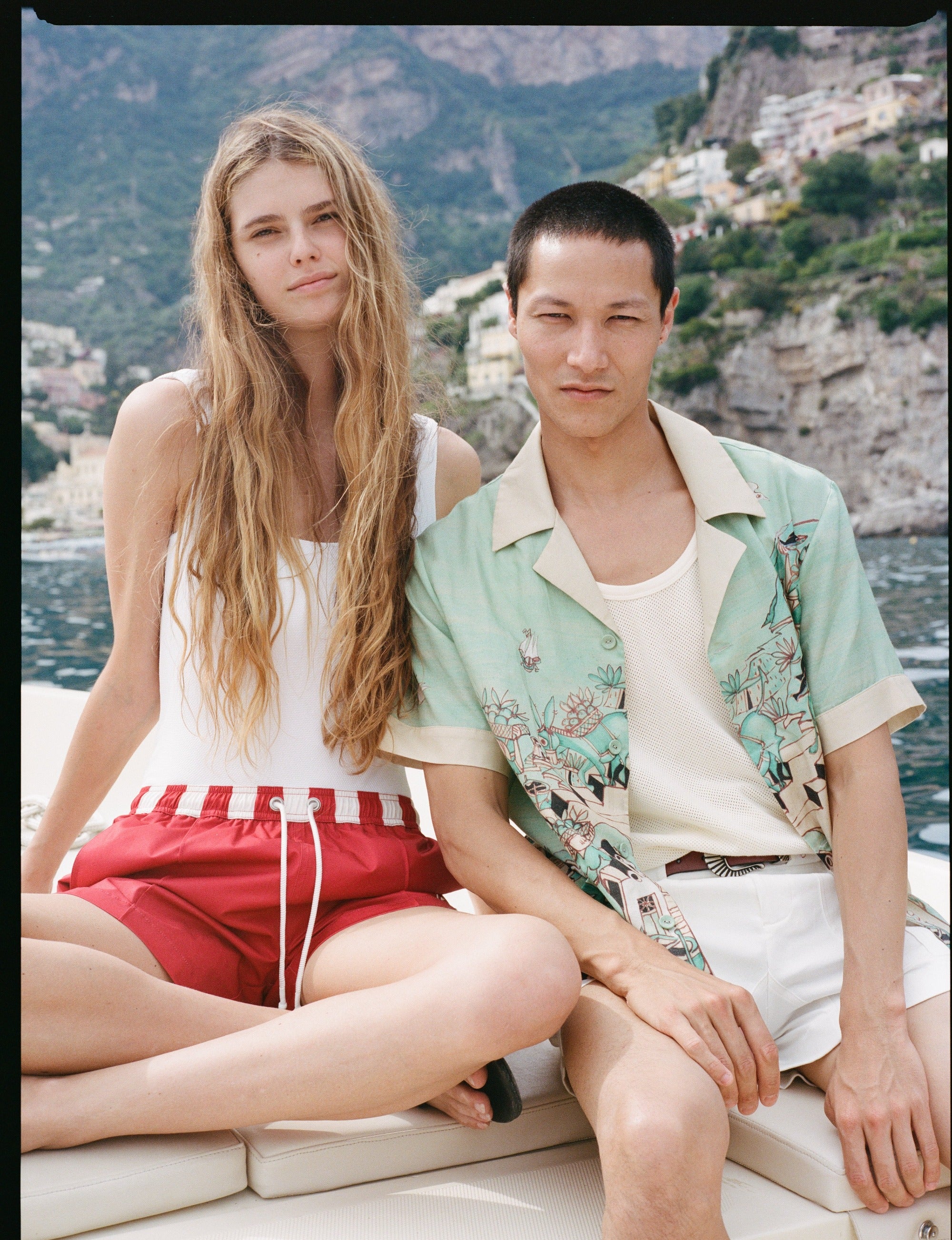 man and woman staring at the camera on a boat with the positano landscape in the background