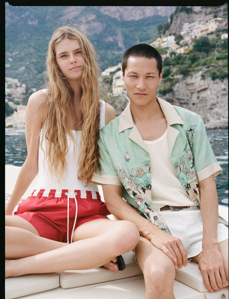 man and woman staring at the camera on a boat with the positano landscape in the background
