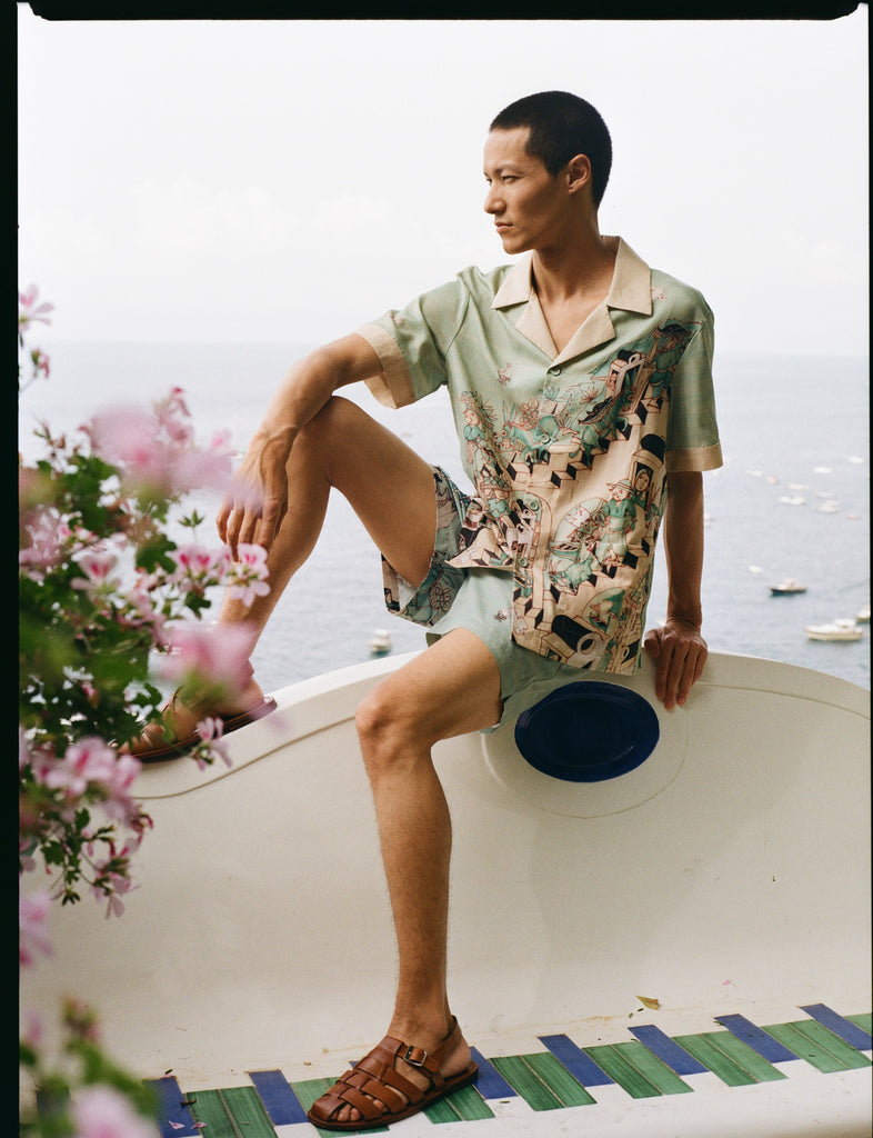 Male model wearing full set sitting along a wall with his leg up