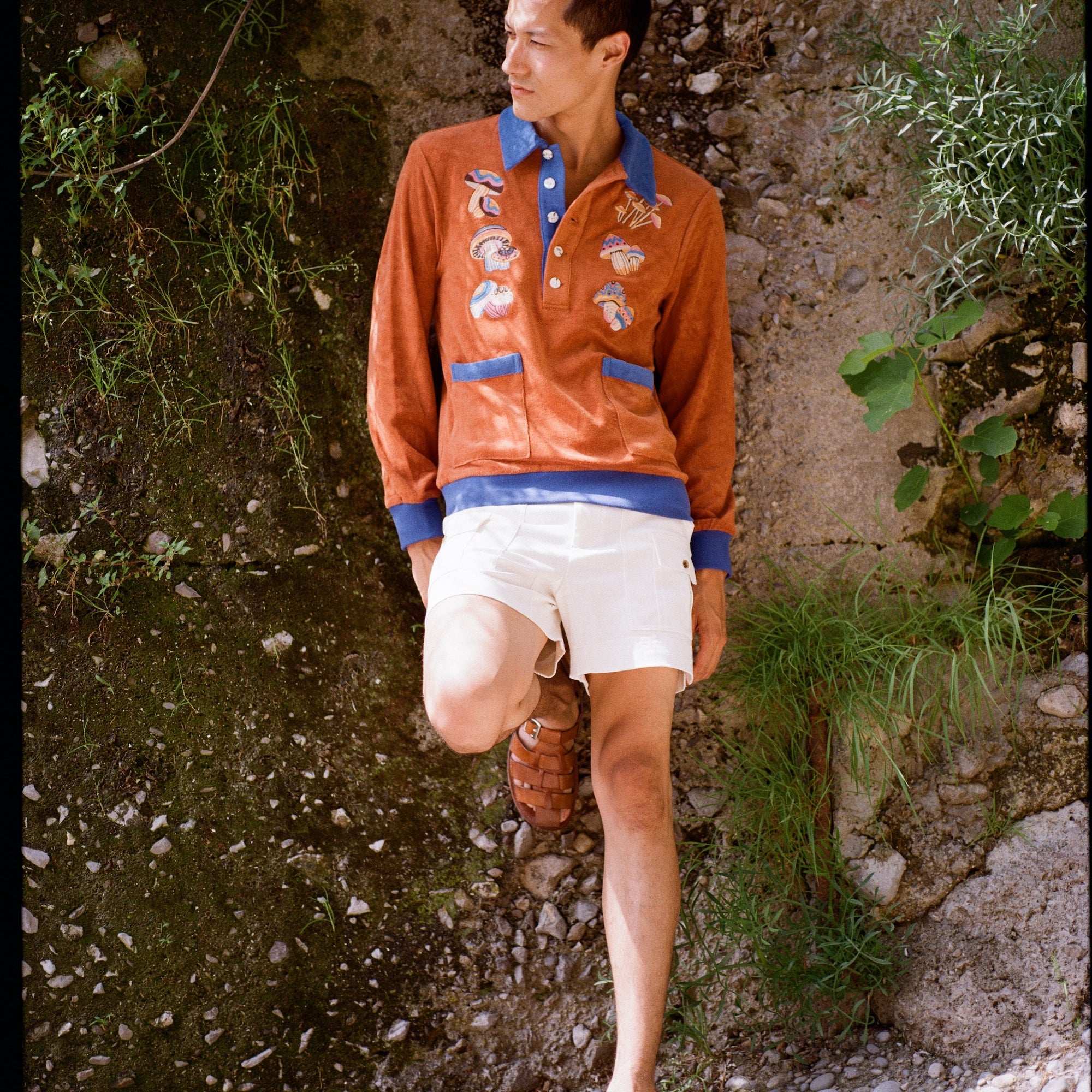 male model standing in disco fungi cabana and stowaway shorts leaning on a natural wall