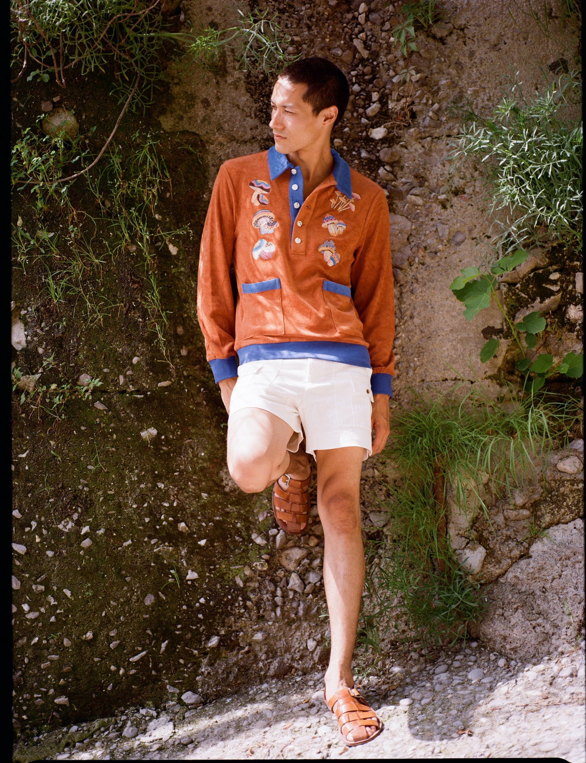male model standing in disco fungi cabana and stowaway shorts leaning on a natural wall