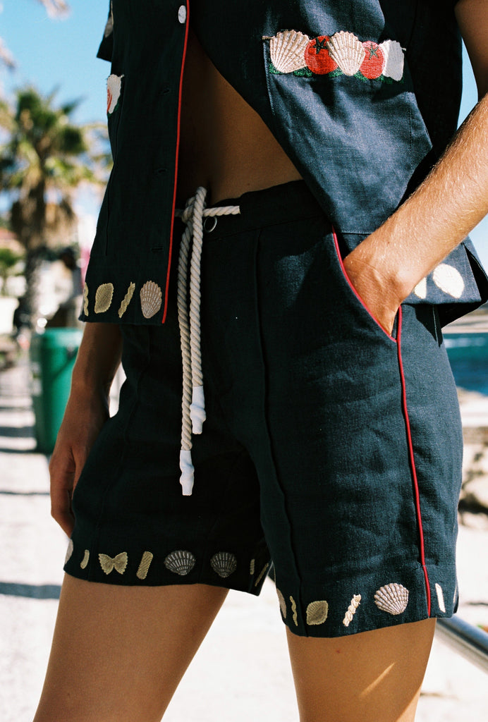 cropped image of woman wearing vongole linen shorts with hanging drawstring and half unbuttoned crop cut matching shirt