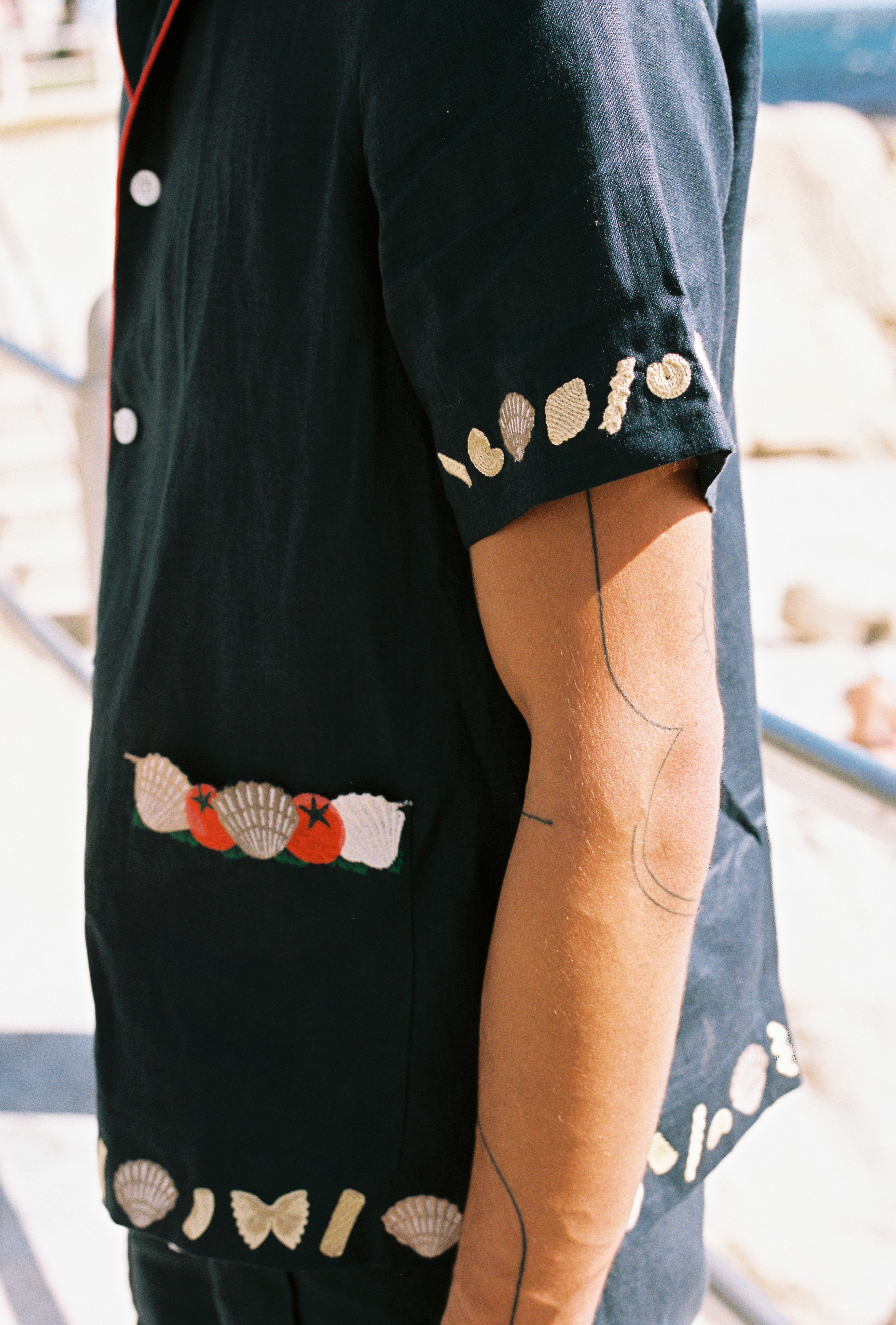 Close up of right sleeve on male model showing the pasta and shell embroidery