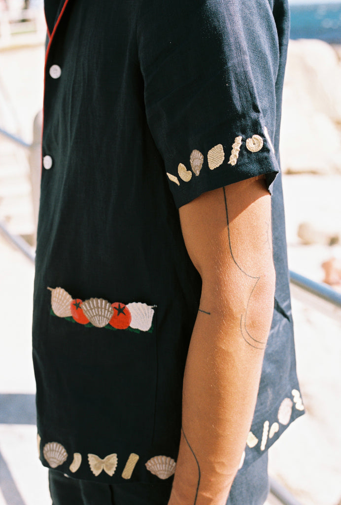 Close up of right sleeve on male model showing the pasta and shell embroidery