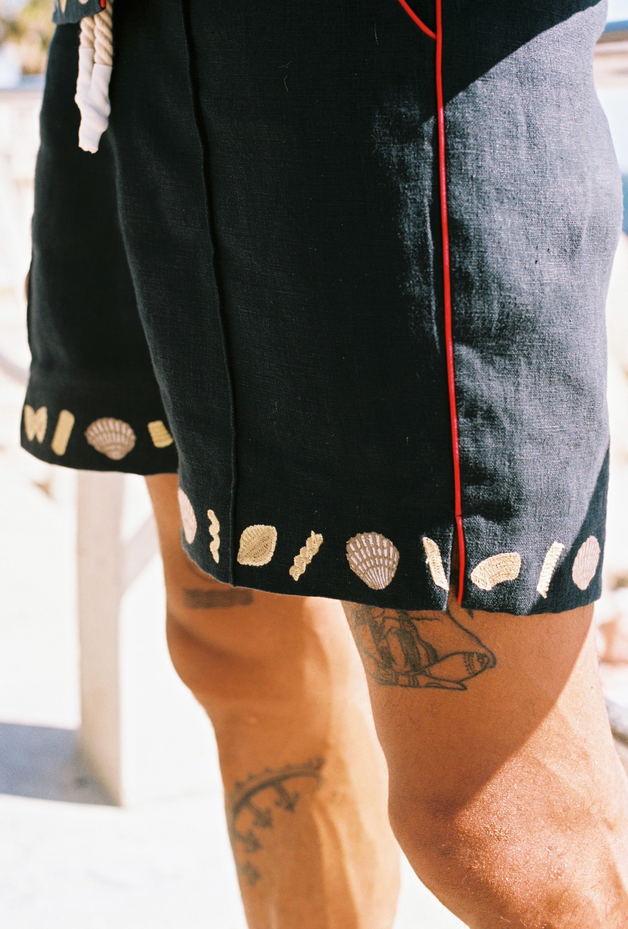 Close up of man wearing vongole linen shorts with tattoos showing on his legs