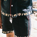 Man places hand inside shirt pocket showing the embroidered clams and tomatoes lining the outside of the pocket