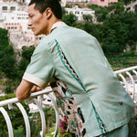 Man leans over balcony looking out onto the ocean in the Tombolo Liguori silk set