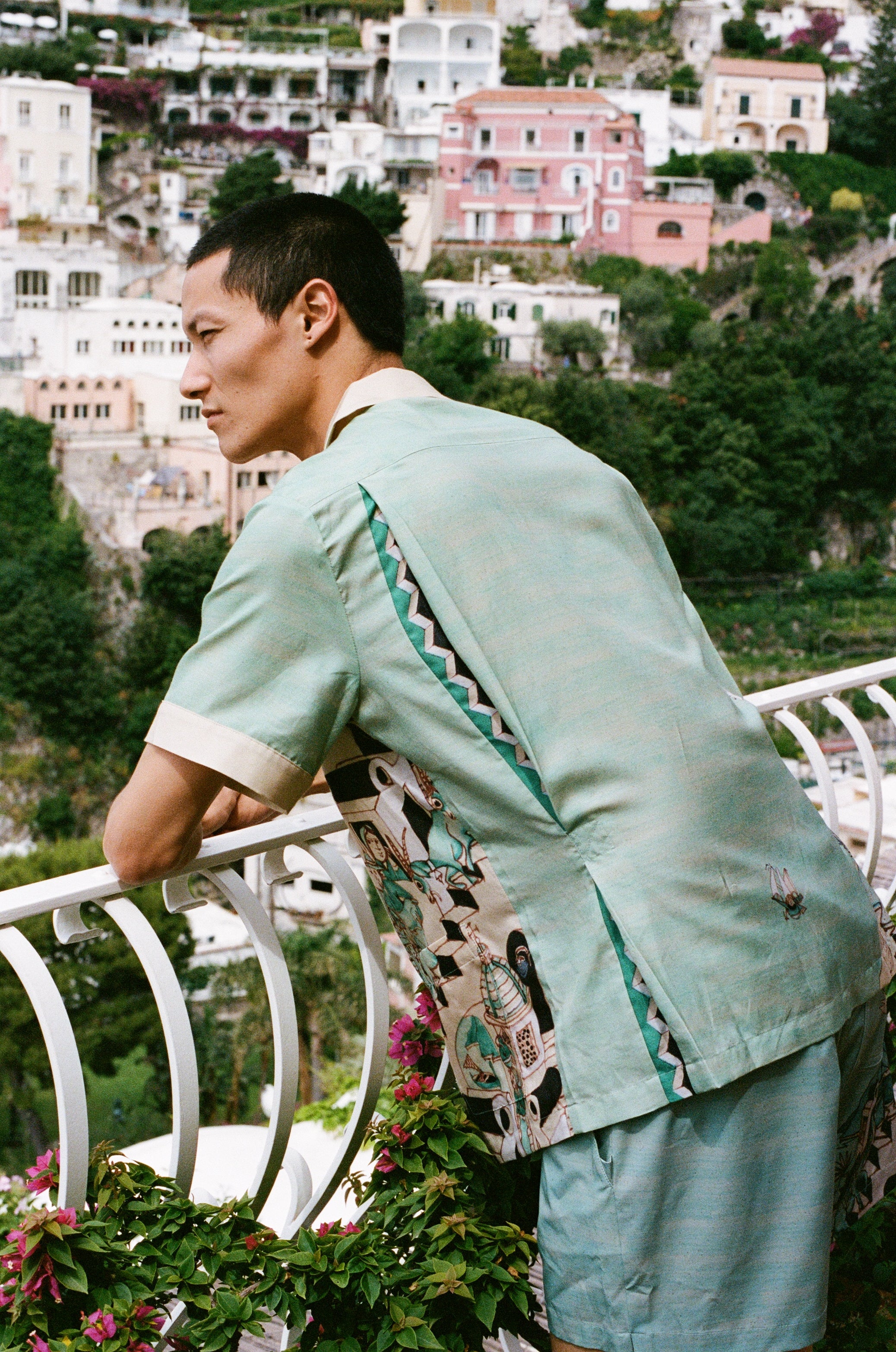 Man leans over balcony looking out onto the ocean in the Tombolo Liguori silk set