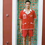 Man wearing red Le Sirenuse matching set standing in green tiled shower