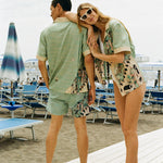 Woman leans on Man's shoulder smiling at the camera, wearing matching shirts and swim trunks