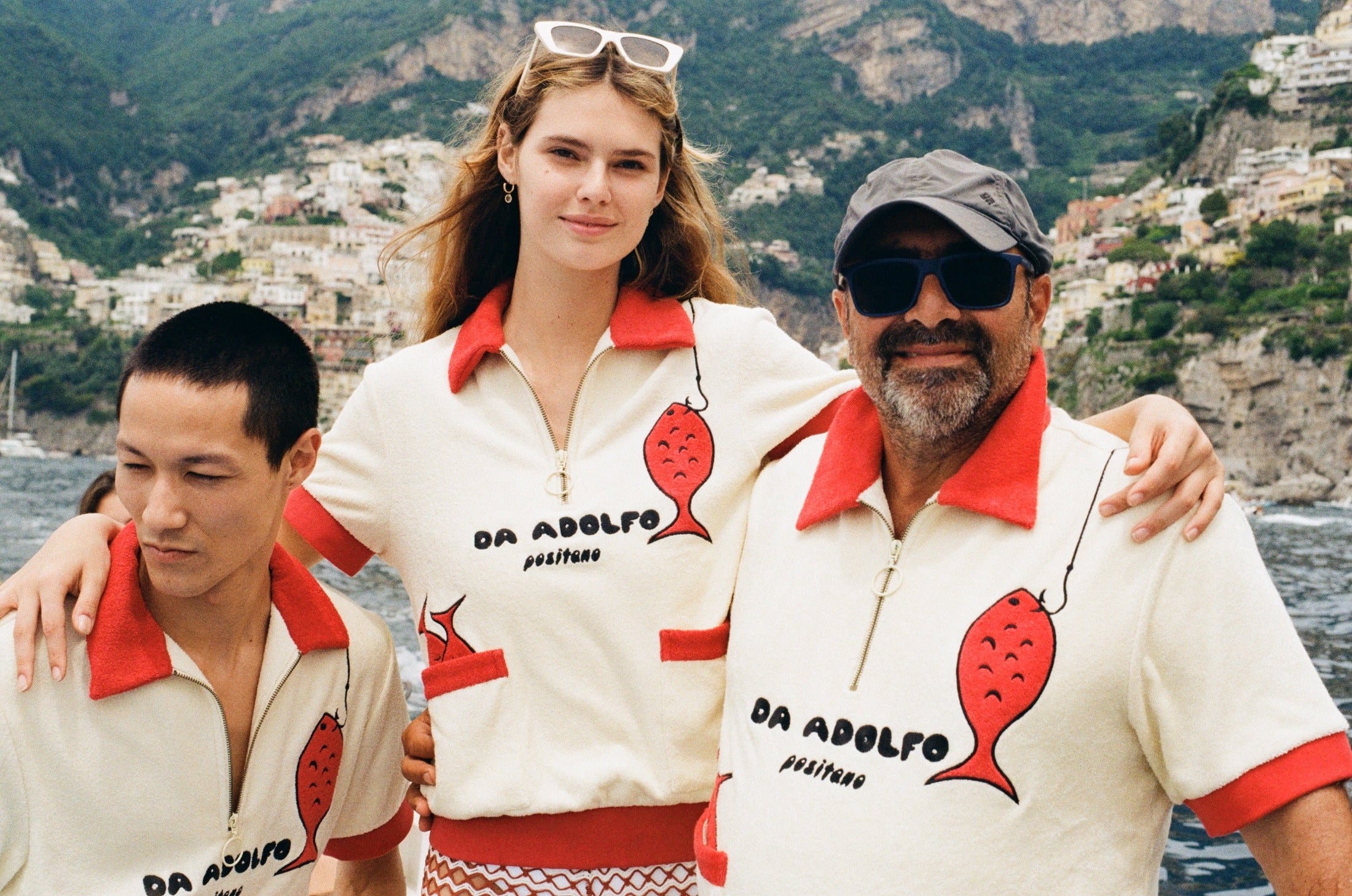 Two men and a woman wear the matching shirt on a boat with Positano in the background