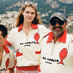 Two men and a woman wear the matching shirt on a boat with Positano in the background