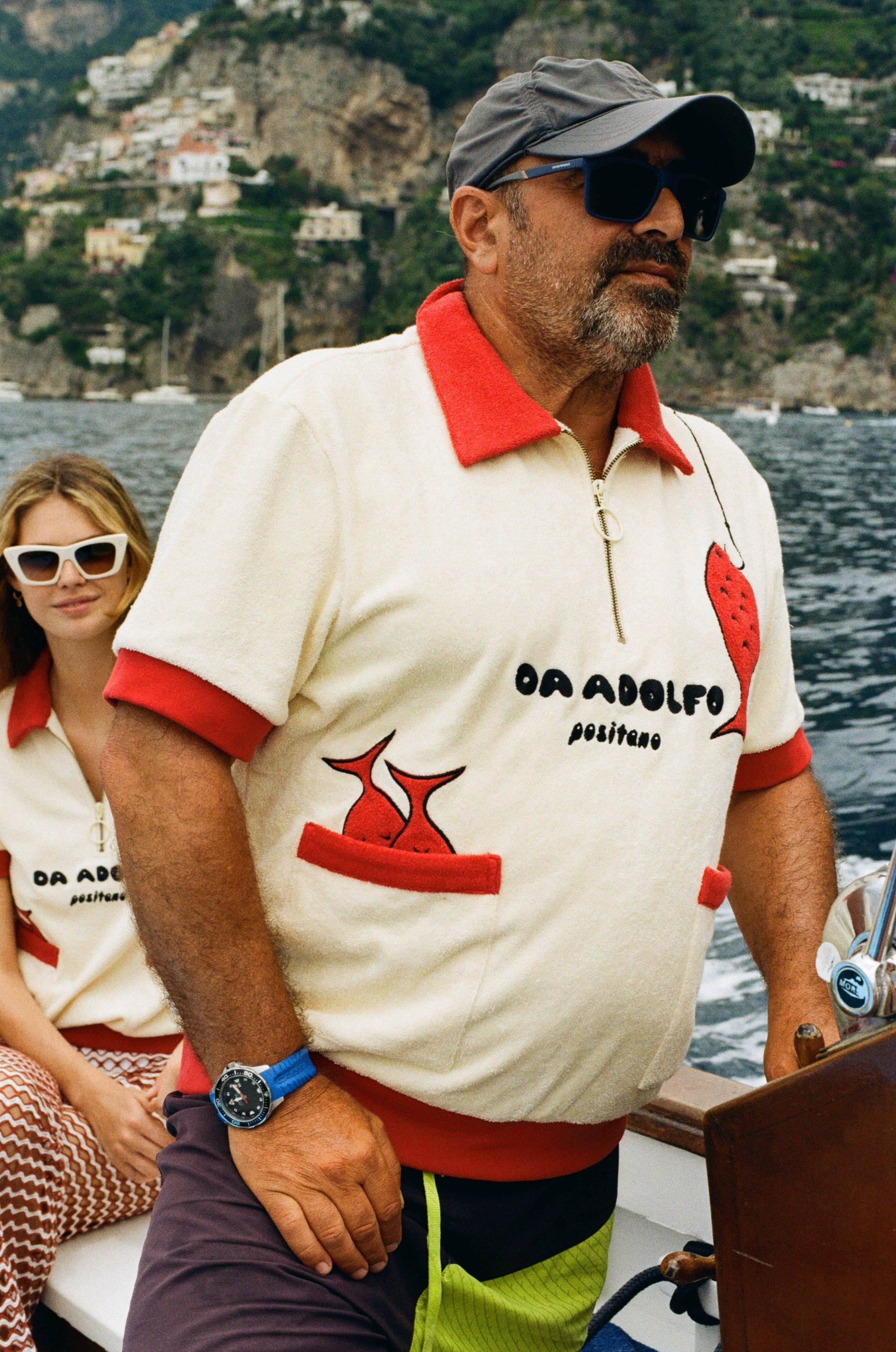 Man wearing baseball cap driving a boat while wearing the Tombolo Da Adolfo shirt
