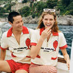 Man and woman wearing matching Da Adolfo Tombolo terry cloth shirts on a boat with the Amalfi landscape in the background