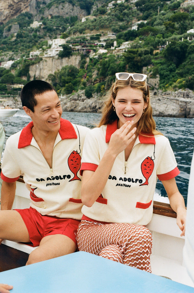Man and woman wearing matching Da Adolfo Tombolo terry cloth shirts on a boat with the Amalfi landscape in the background