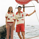 Woman and Man wearing the Da Adolfo shirts while standing on the dock next to the Da Adolfo restaurant sign, a red fish reflected in the embroidery