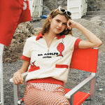 Girl smiling at camera while sitting in red chair wearing Da Adolfo shirt