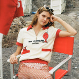 Girl smiling at camera while sitting in red chair wearing Da Adolfo shirt