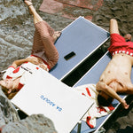 Birdseye shot of man and woman sunbathing in loungechairs with Da Adolfo printed on the sun umbrella