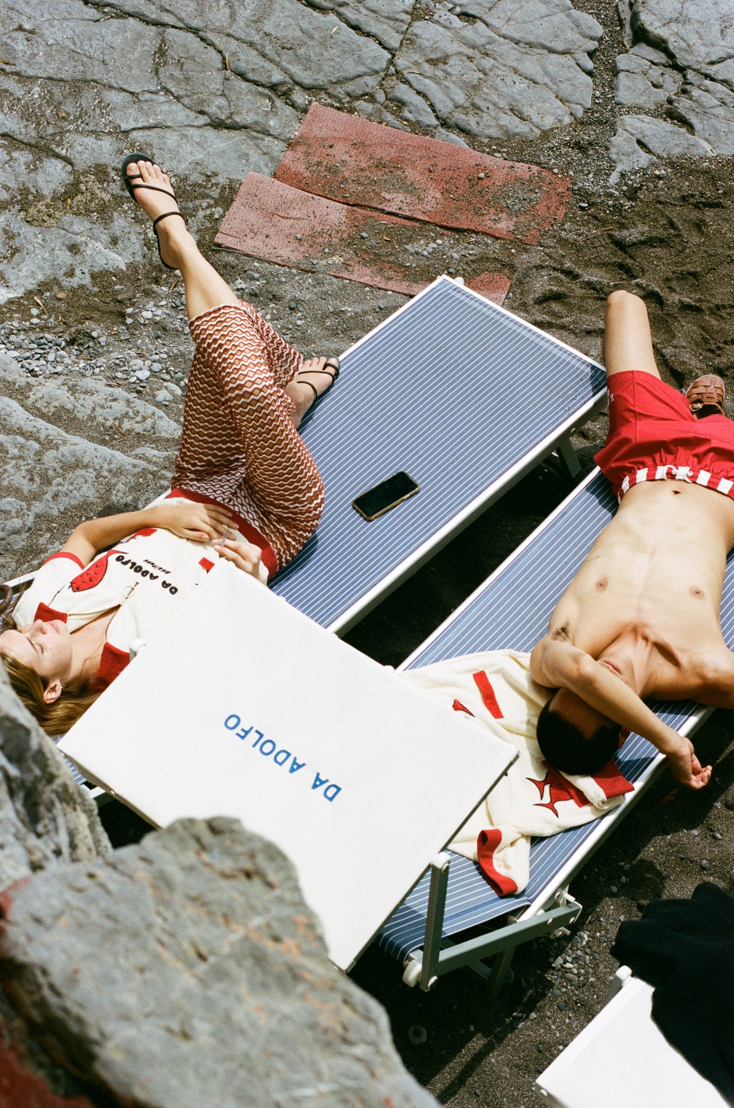 Birdseye shot of man and woman sunbathing in loungechairs with Da Adolfo printed on the sun umbrella