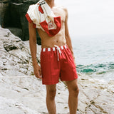 Man wearing Le Sirenuse red swim trunks with Da Adolfo shirt draped over his left shoulder