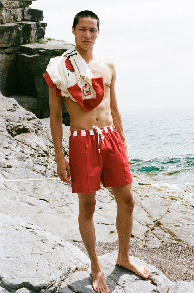 Man wearing Le Sirenuse red swim trunks with Da Adolfo shirt draped over his left shoulder
