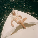 Man lounging on the bow of a white boat under the sun, wearing the matching 'Crouching Tiger' Cabana Set. He reclines with one arm behind his head and the other holding a can, surrounded by shimmering dark  ocean water.