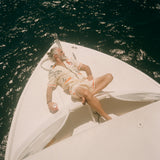 Man lounging on the bow of a white boat under the sun, wearing the matching 'Crouching Tiger' Cabana Set. He reclines with one arm behind his head and the other holding a can, surrounded by shimmering dark  ocean water.