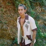 Male model walking in front of rocky wall wearing full 'Tombarola' cabana set with shirt unbuttoned.