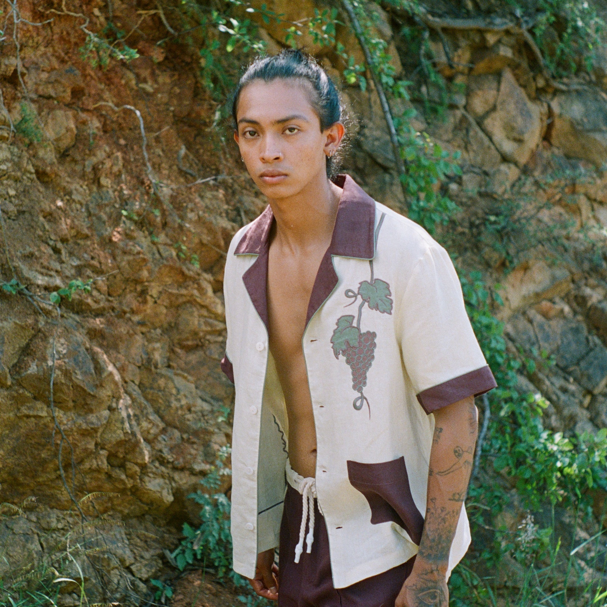 Male model walking in front of rocky wall wearing full 'Tombarola' cabana set with shirt unbuttoned.