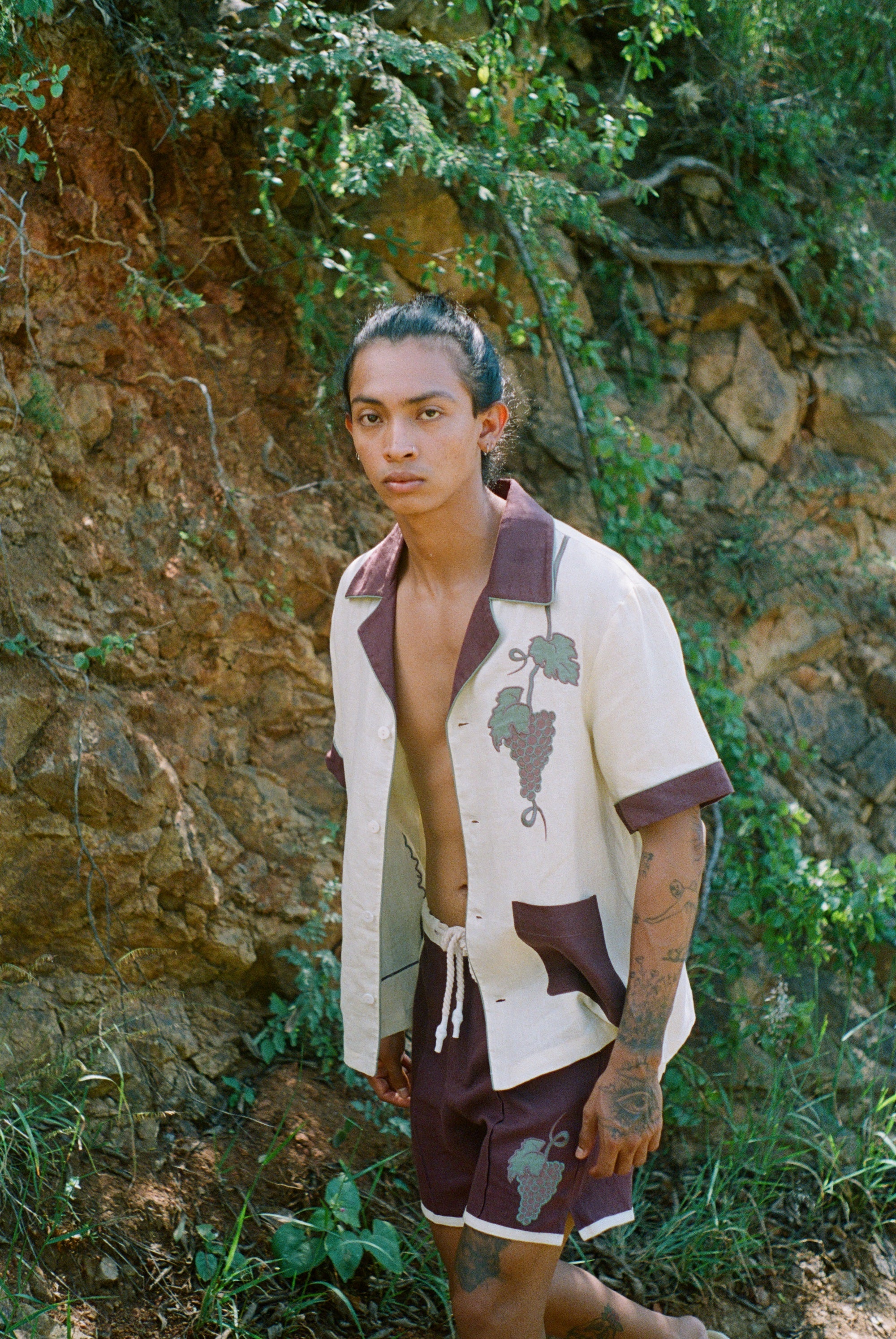 Male model walking in front of rocky wall wearing full 'Tombarola' cabana set with shirt unbuttoned.