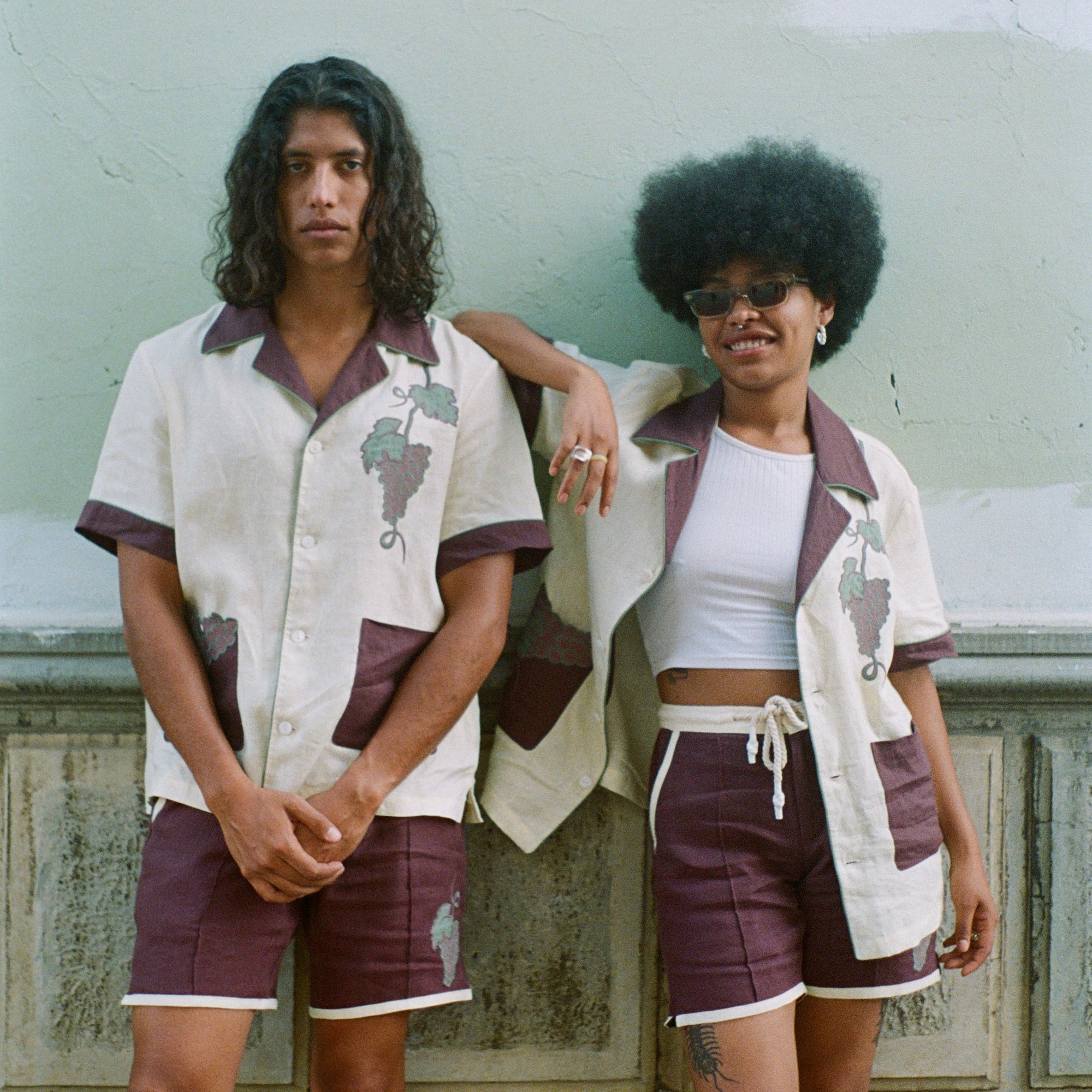 Male model and female model standing together wearing full 'Tombarolo' cabana sets Female model wears shirt unbuttoned over white tank top