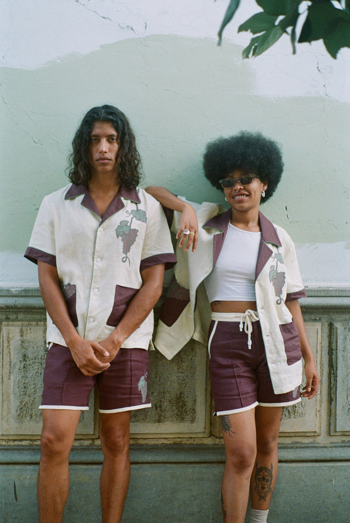 Male model and female model standing together wearing full 'Tombarolo' cabana sets Female model wears shirt unbuttoned over white tank top