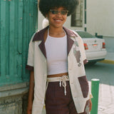 Female model leaning against wall wearing full 'Tombarolo' cabana set. Shirt is open over a white tank top.