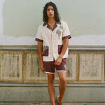 Man leaning against dilapidated urban wall wearing full 'Tombarolo' cabana set with flip flops and necklace on