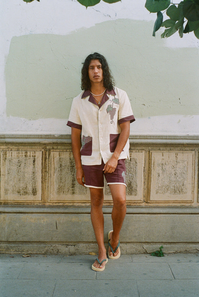 Man leaning against dilapidated urban wall wearing full 'Tombarolo' cabana set with flip flops and necklace on
