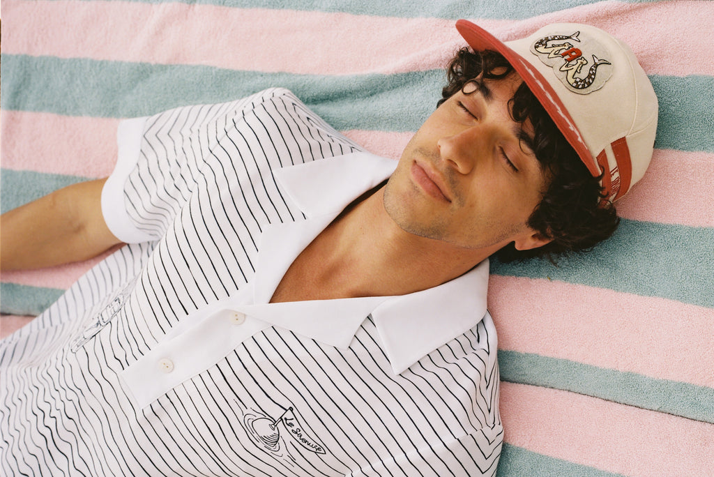 Man lying down with eyes closed wearing Corsa shirt and sirenuse cap