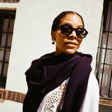 woman looking off to the right wearing black framed sunglasses, wearing a white sweater and a navy sweater around her neck 