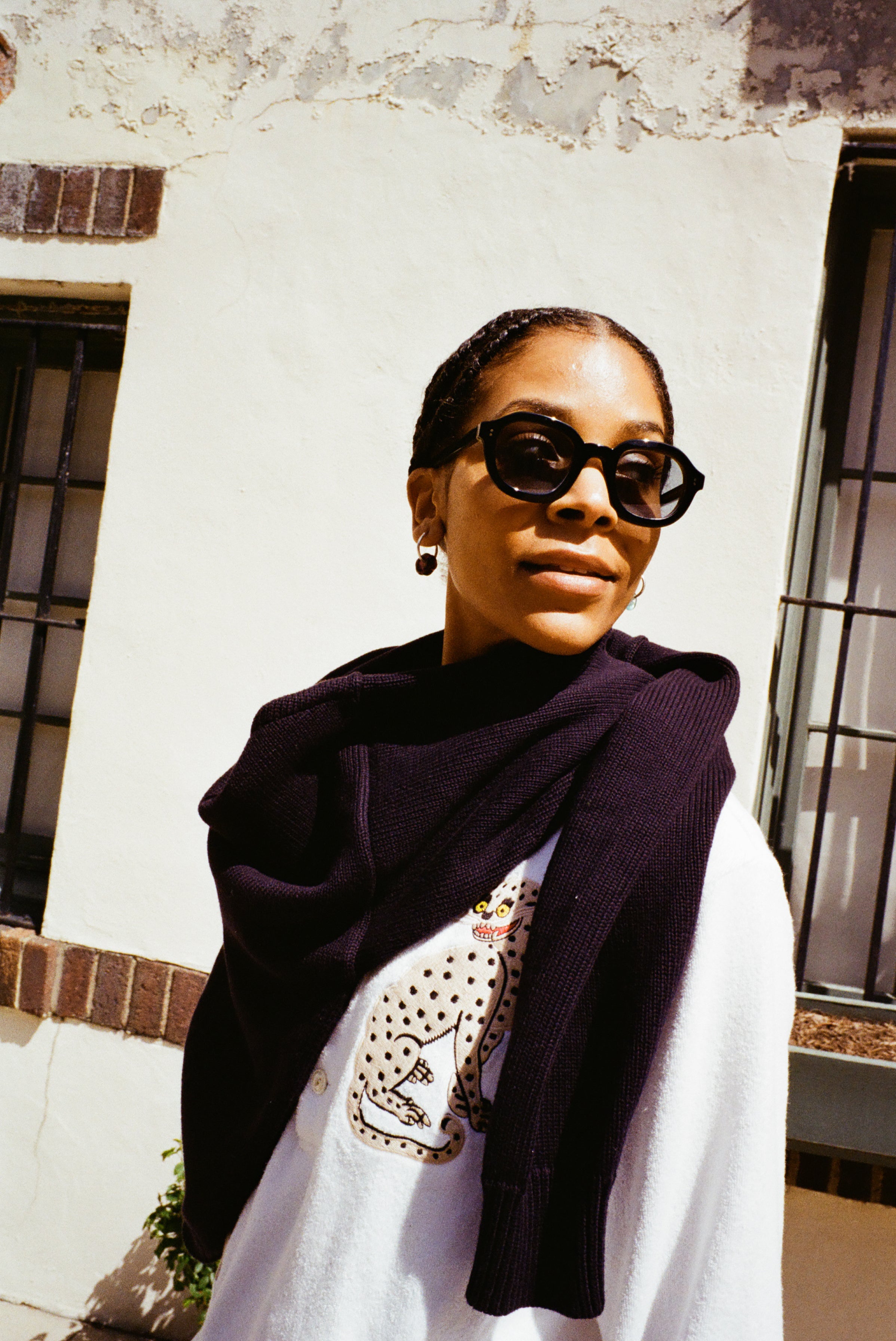 woman looking off to the right wearing black framed sunglasses, wearing a white sweater and a navy sweater around her neck 