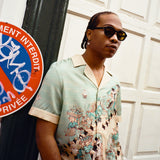 Young male model wearing Lesca Lunetier X Tombolo lenses in charcoal in addition to the "Le Sirenuse by Lucio Liguori" Hawaiian on the streets of Paris standing next to a No Parking sign written in french.