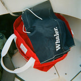 Navy board shorts with white contrast stitching and white 'Whaler' text on the leg, resting on top of a red canvas tote bag.