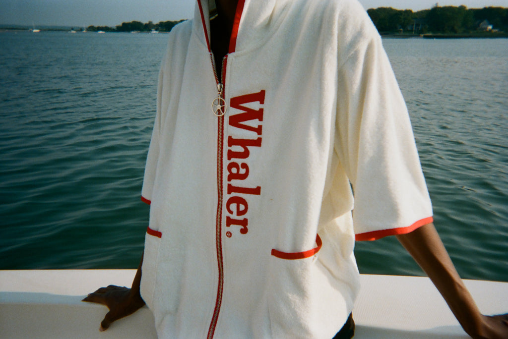 Close-up of woman wearing the white hooded beach towel top with red trim and vertical 'Whaler' text.